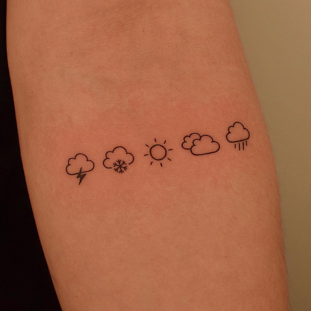 Minimalist weather symbol tattoos on an arm including a storm cloud with lightning.