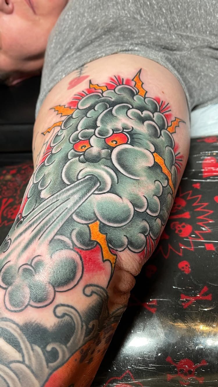 Storm cloud tattoo with lightning bolts and a face on a person's arm.