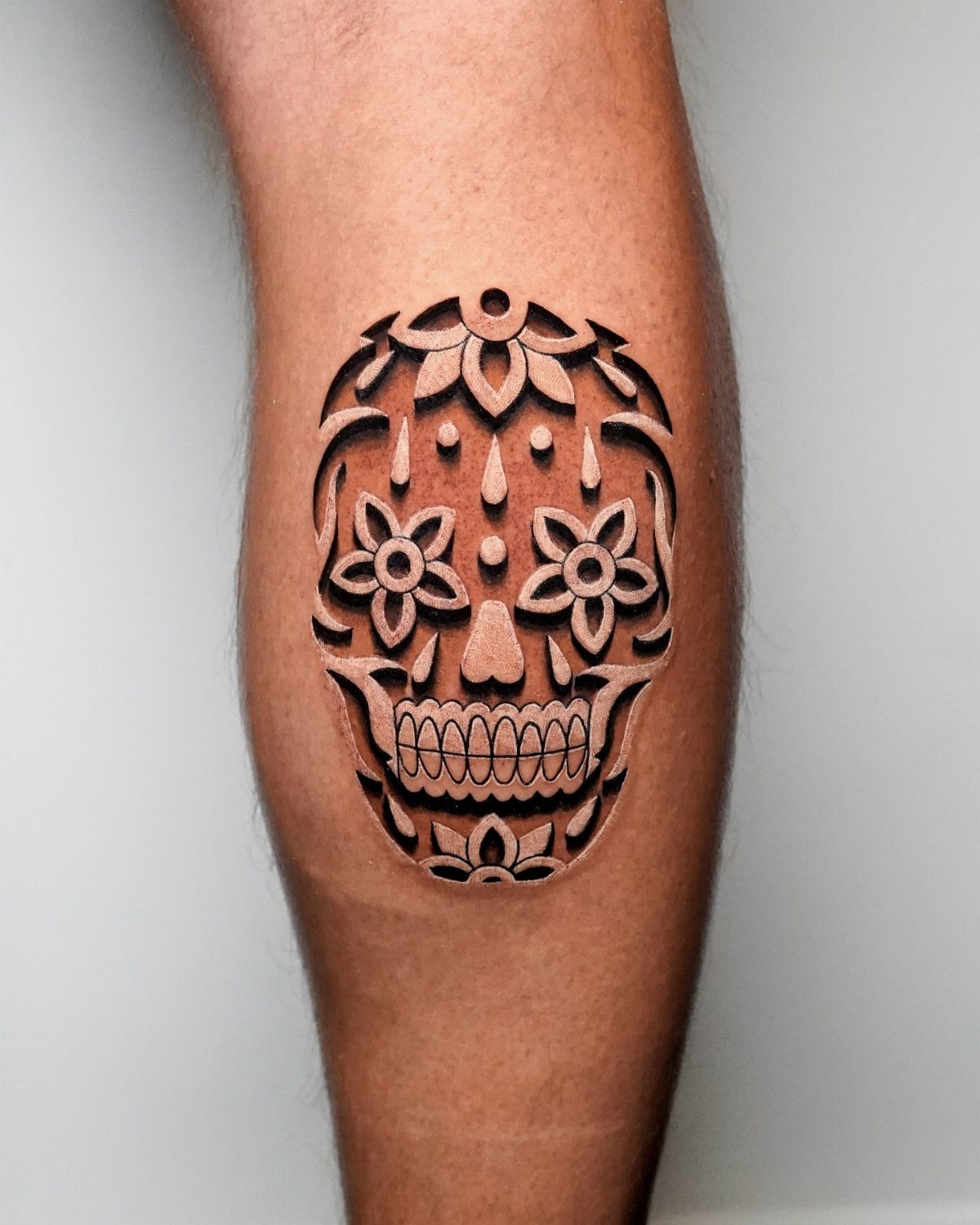3D sugar skull tattoo with floral details on a person's forearm or calf