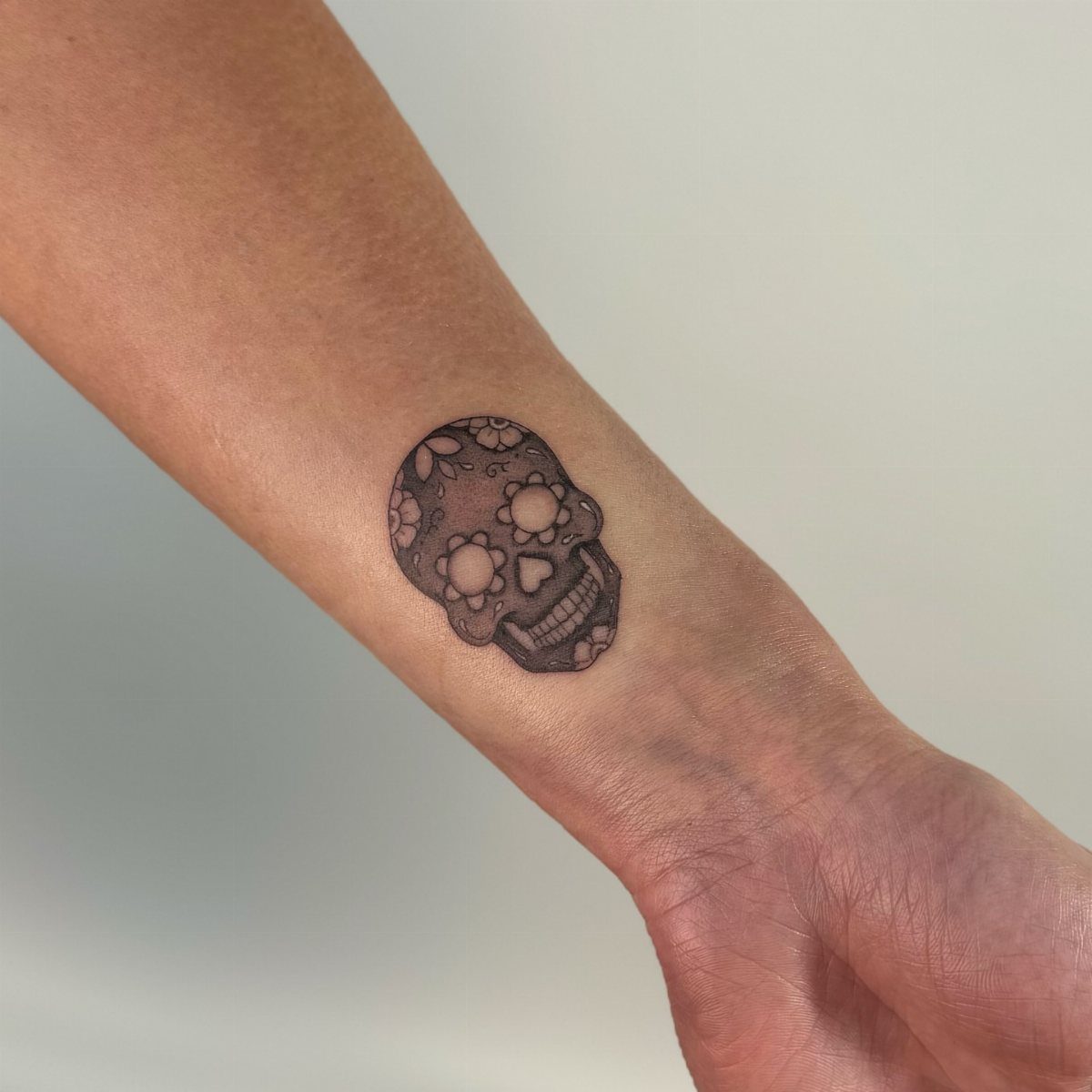 Sugar skull tattoo on a person's inner wrist in black and grey ink.