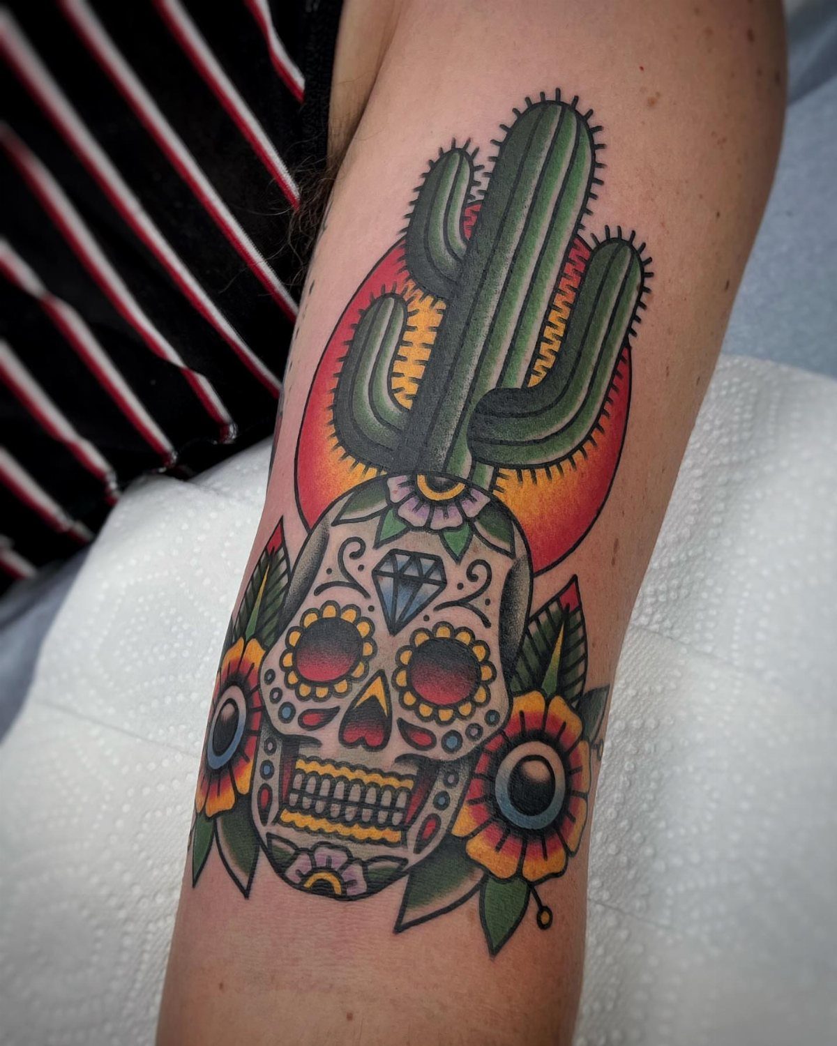 Colorful sugar skull tattoo on a forearm with a cactus and flowers.