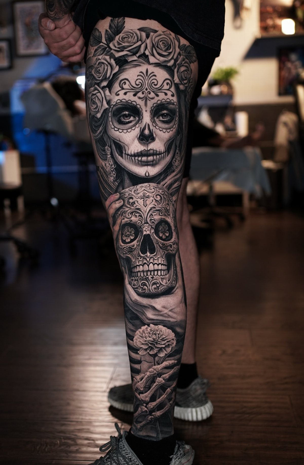 Realistic black and grey sugar skull tattoo with roses on a person's leg.