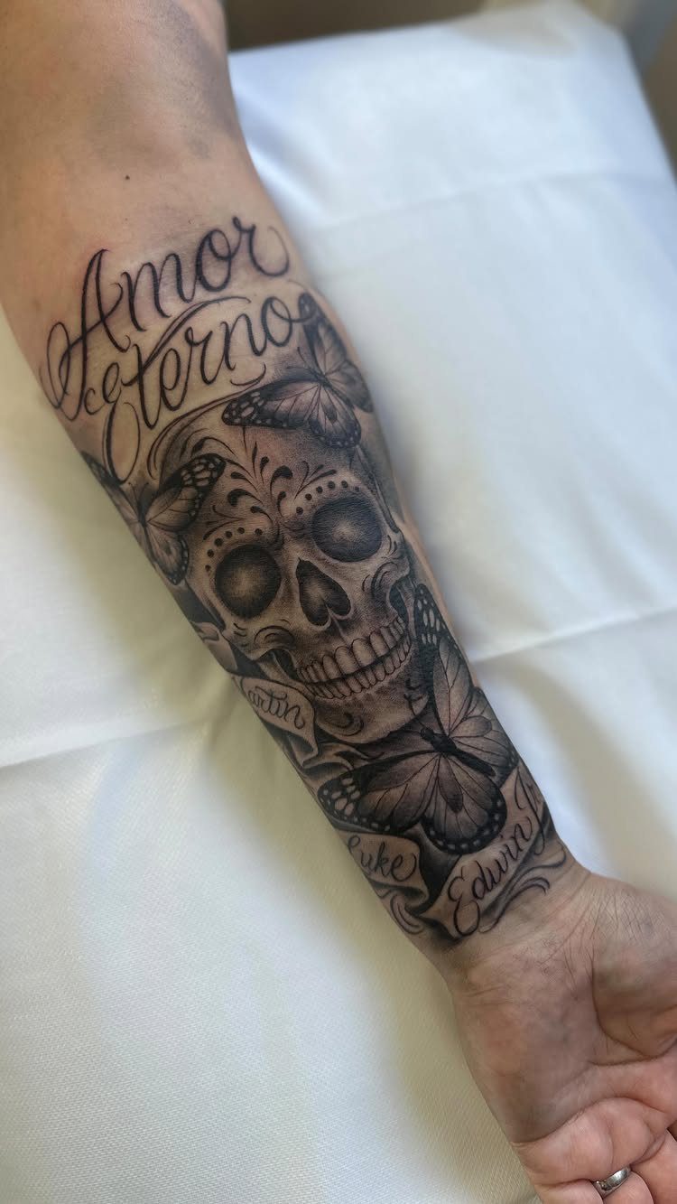 Sugar skull tattoo with butterflies and Amor Eterno text on a forearm