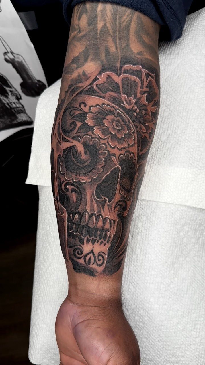 Sugar skull tattoo with flowers on a person's forearm in black and grey ink