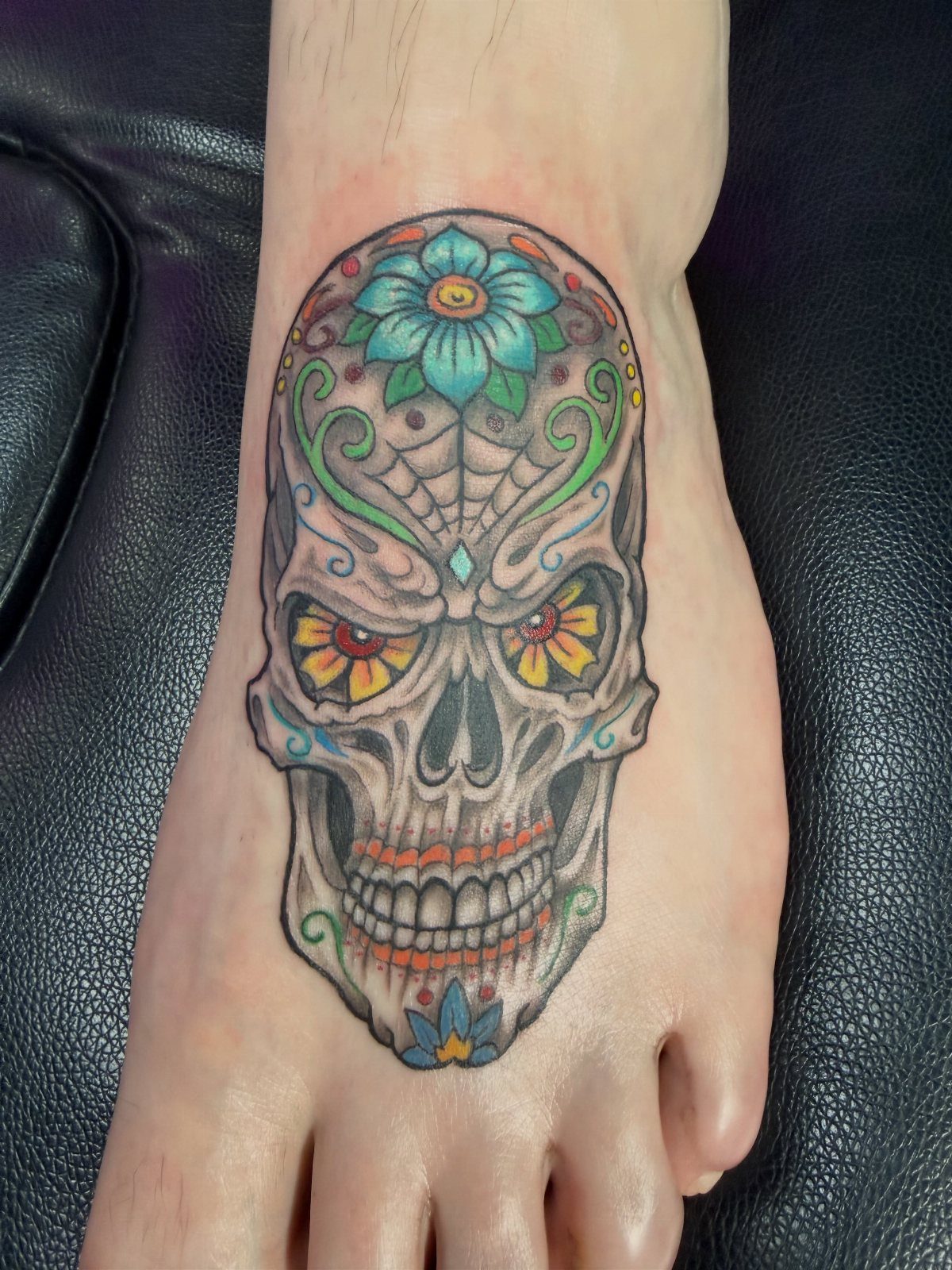 Colorful sugar skull tattoo with flowers on the top of a human foot