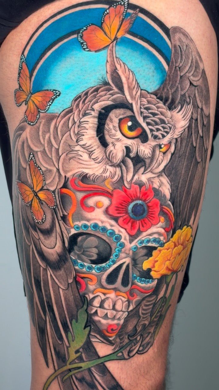 Colorful tattoo of a grey owl perched on a decorated sugar skull with butterflies.