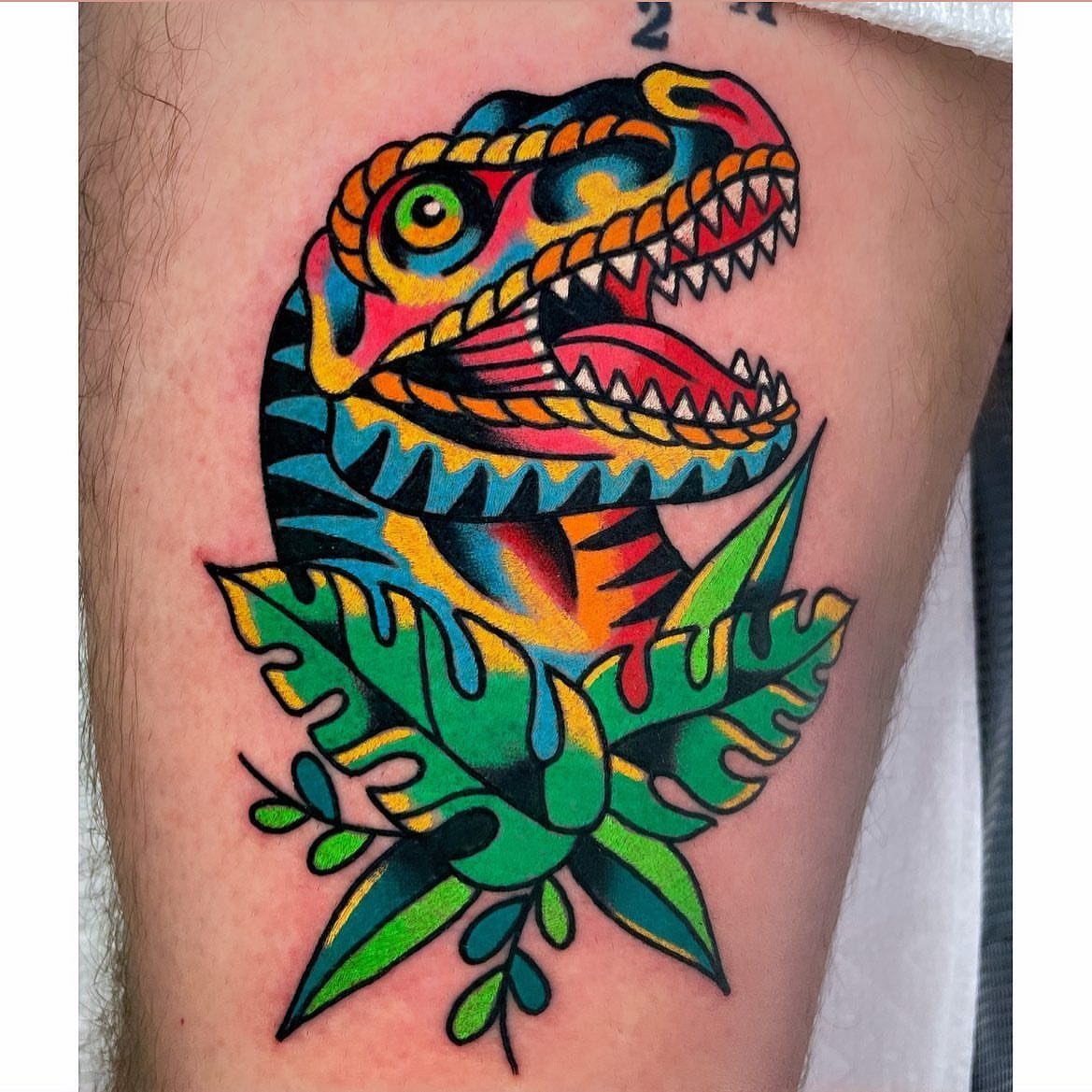 Colorful T-Rex head tattoo with bright hues and green tropical leaves on skin