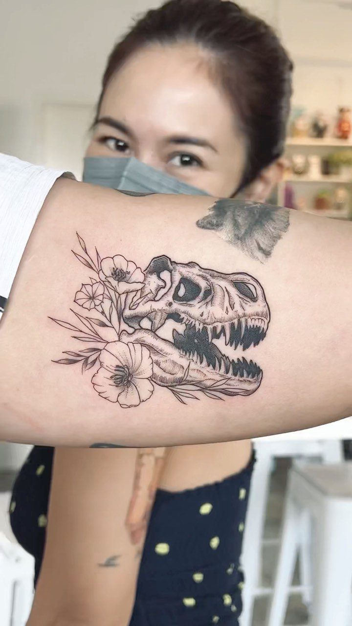 T-Rex skull tattoo with flowers on a person's upper arm