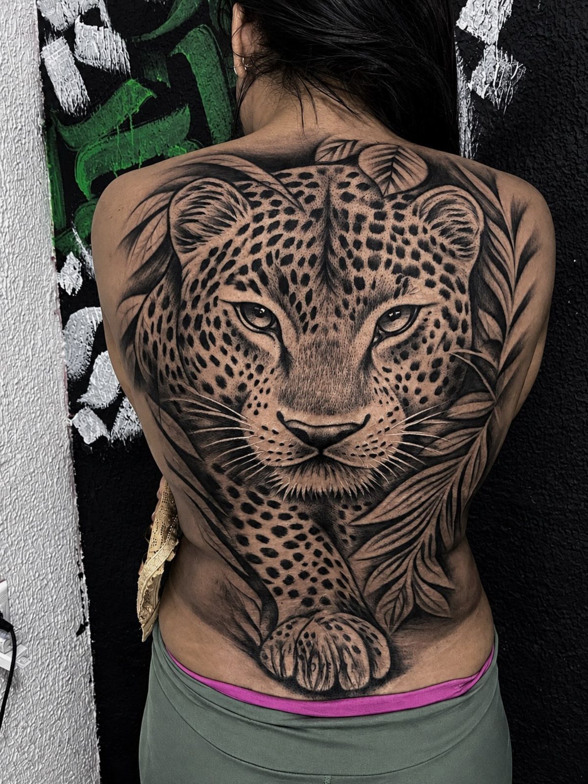 Cheetah face tattoo covering the entire back of a person with detailed spots.