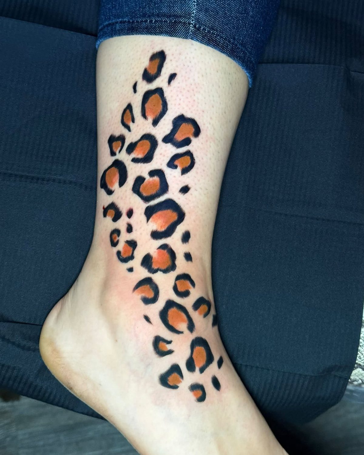 Cheetah print tattoo with orange and black spots on a person's ankle.