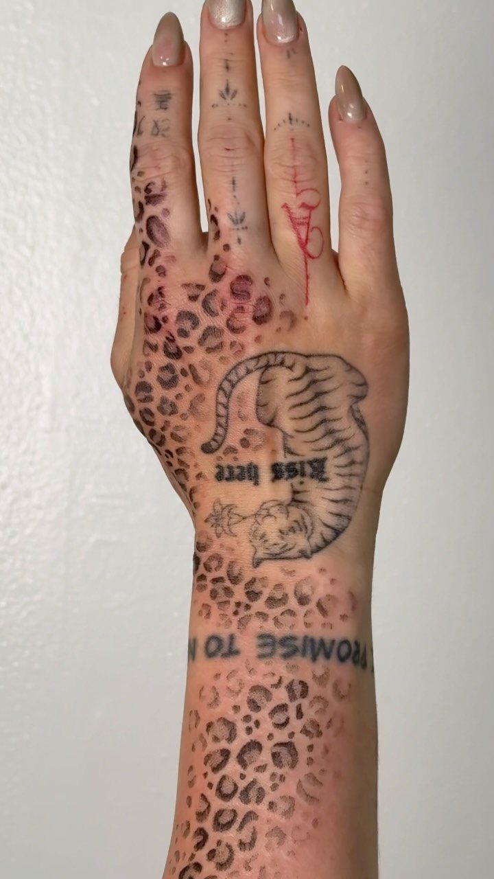 Hand and forearm with cheetah print tattoos and a curled cat illustration.