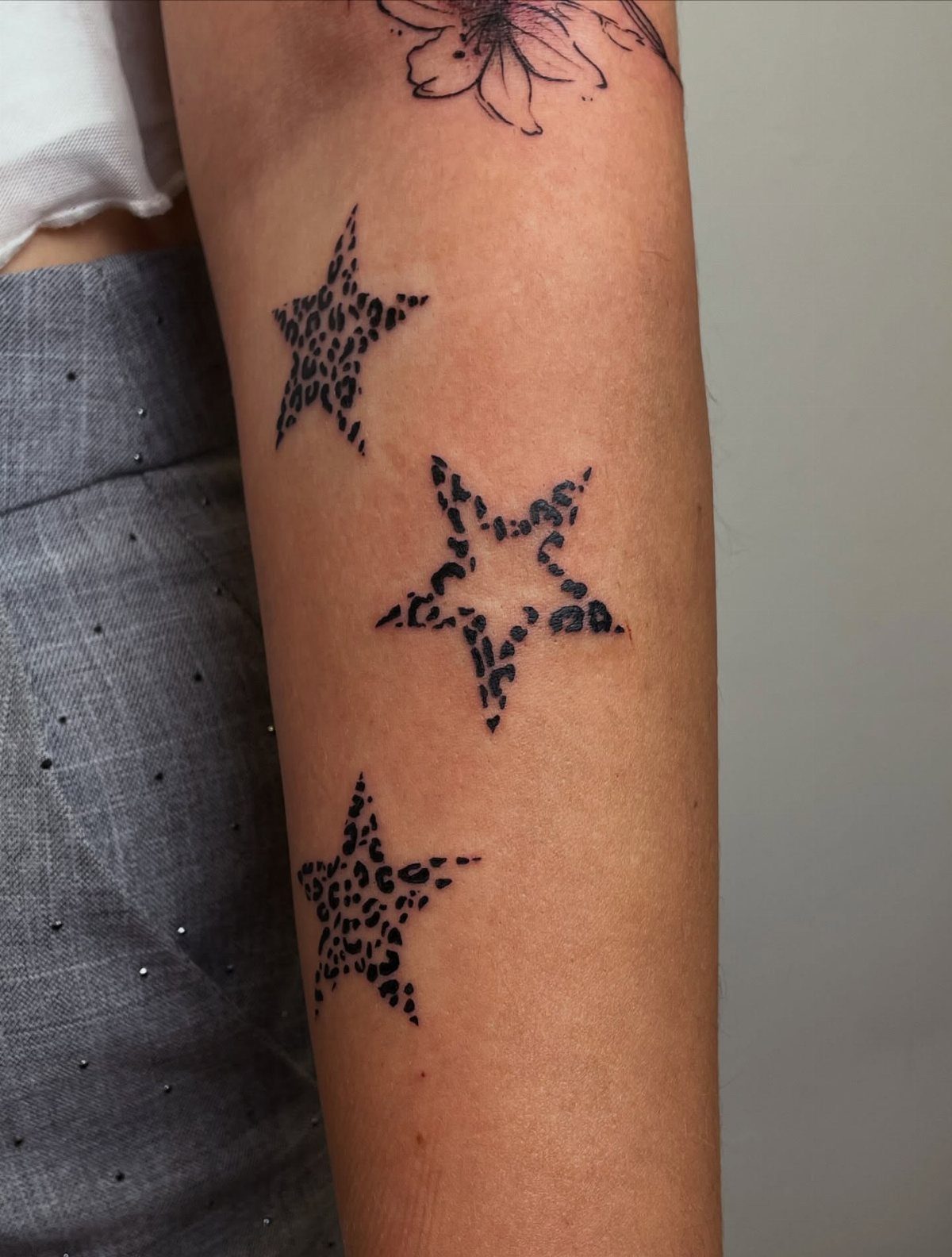 Three star tattoos with cheetah print patterns on a person's forearm.