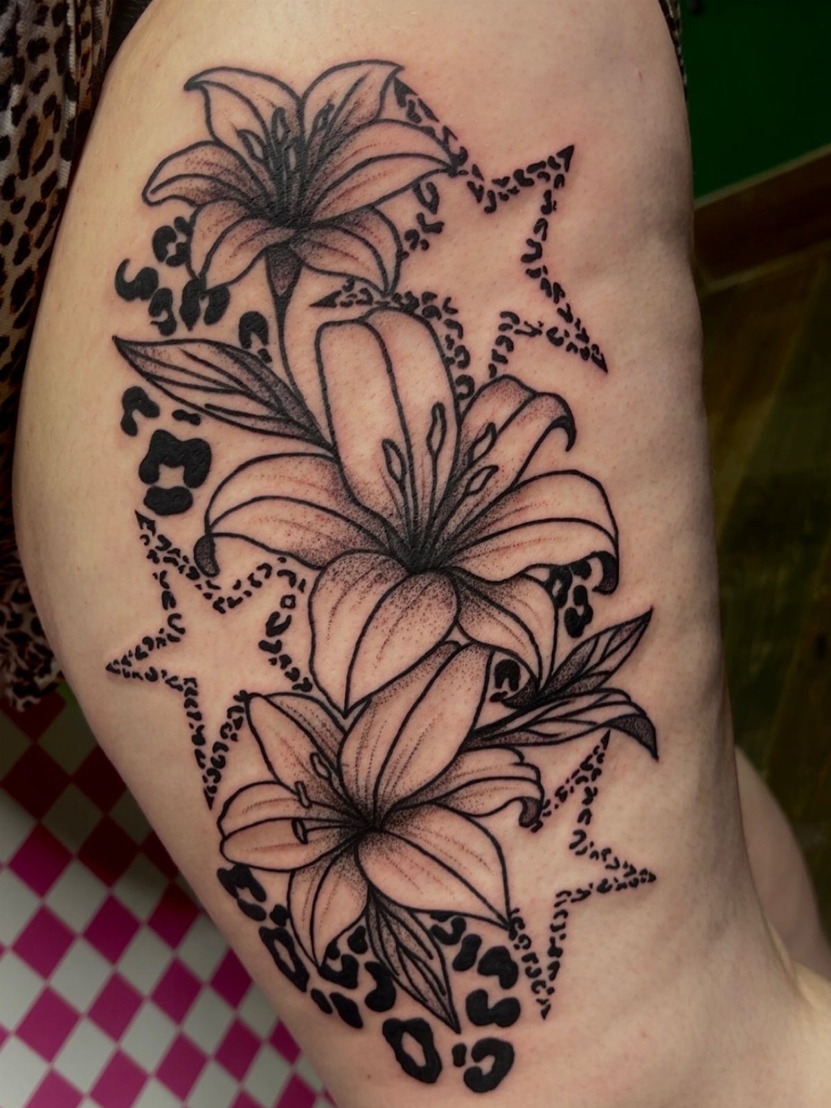 Cheetah print tattoo on a thigh featuring lilies and stars in black ink.