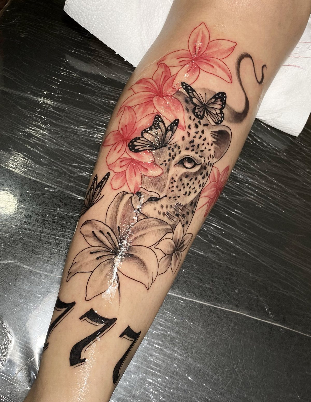 Cheetah face tattoo with pink lilies and butterflies on a person's arm.