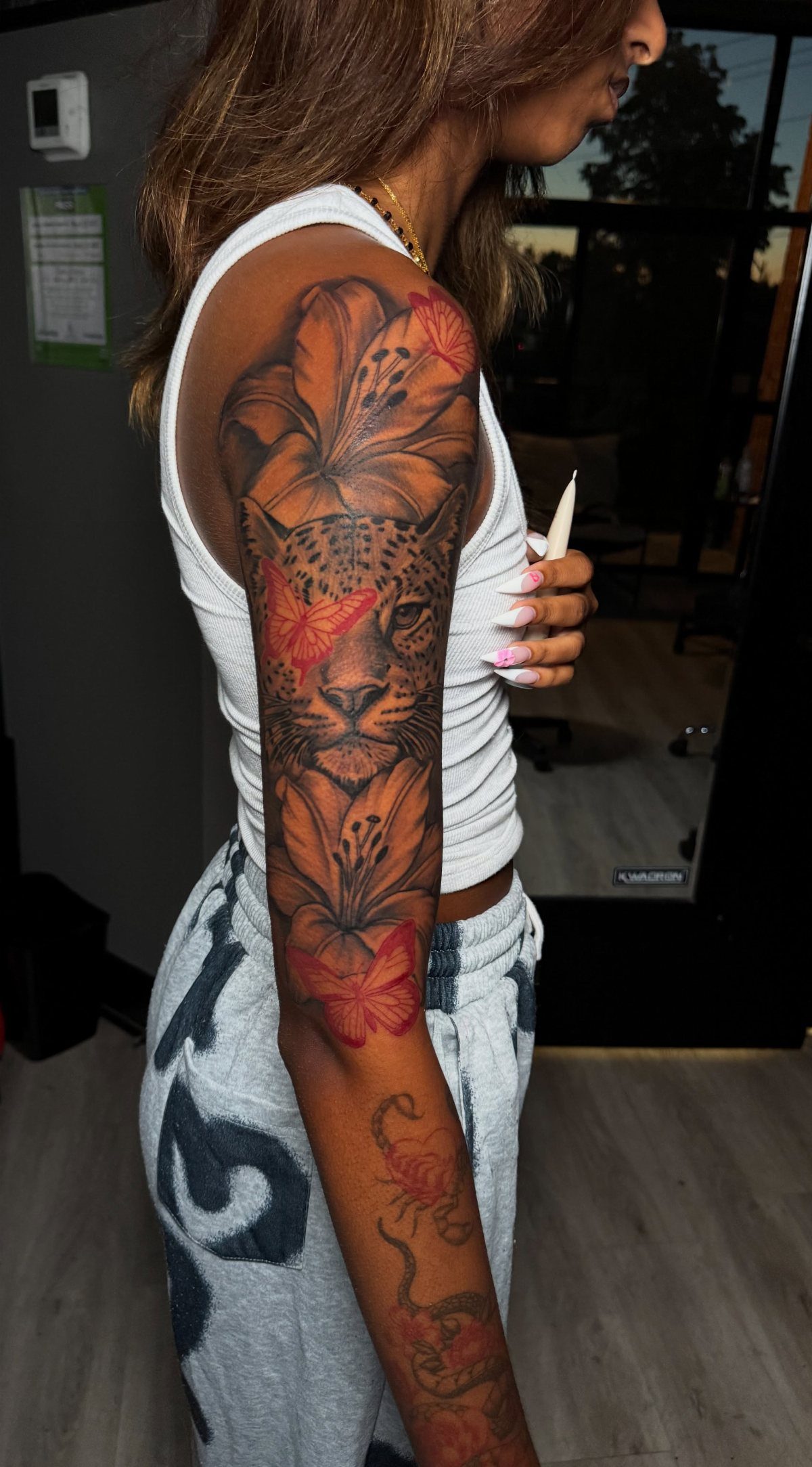 Cheetah face tattoo with red lilies and butterflies on a woman's shoulder and arm.