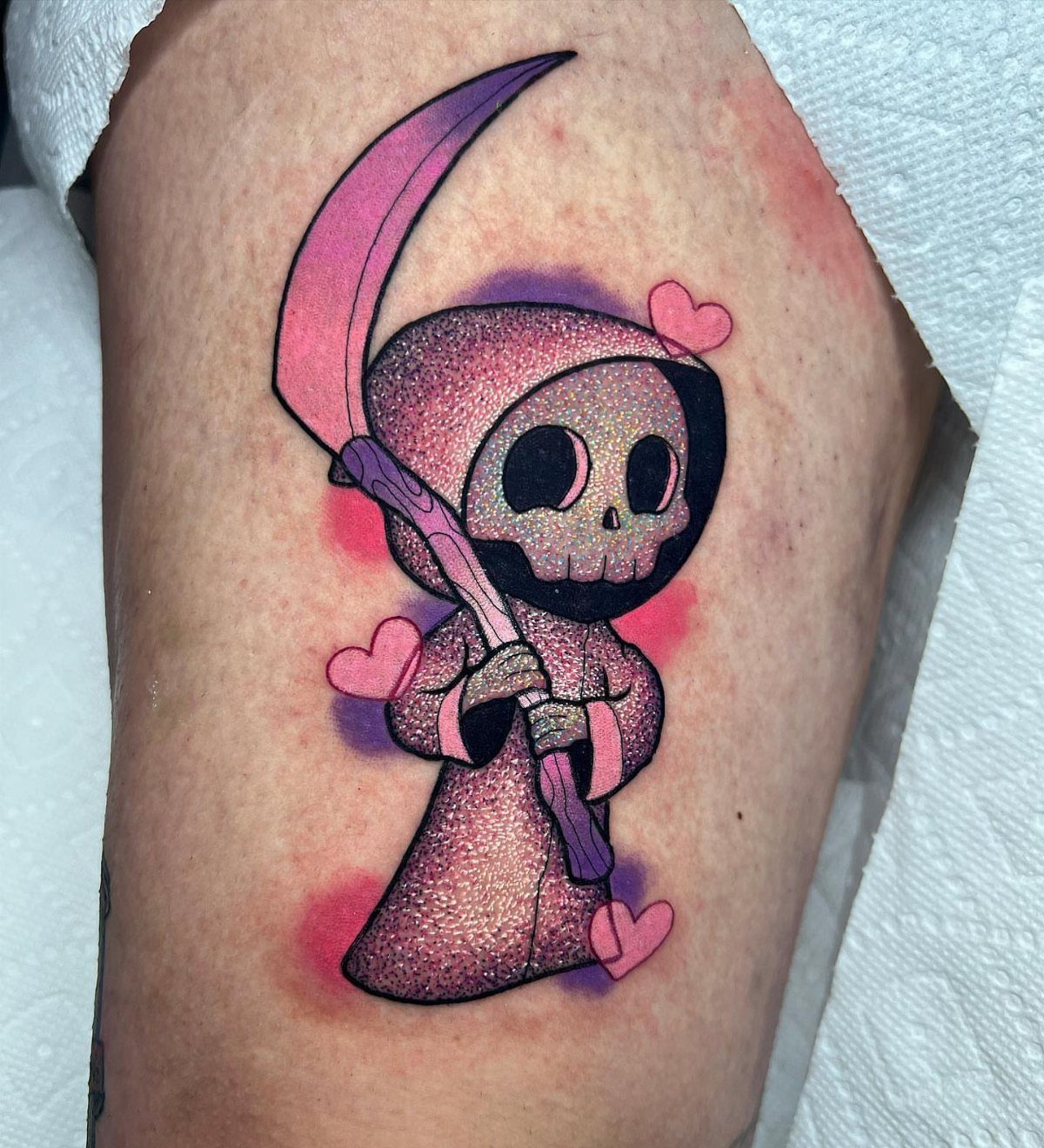 Stylized grim reaper tattoo with a purple robe and pink hearts on skin