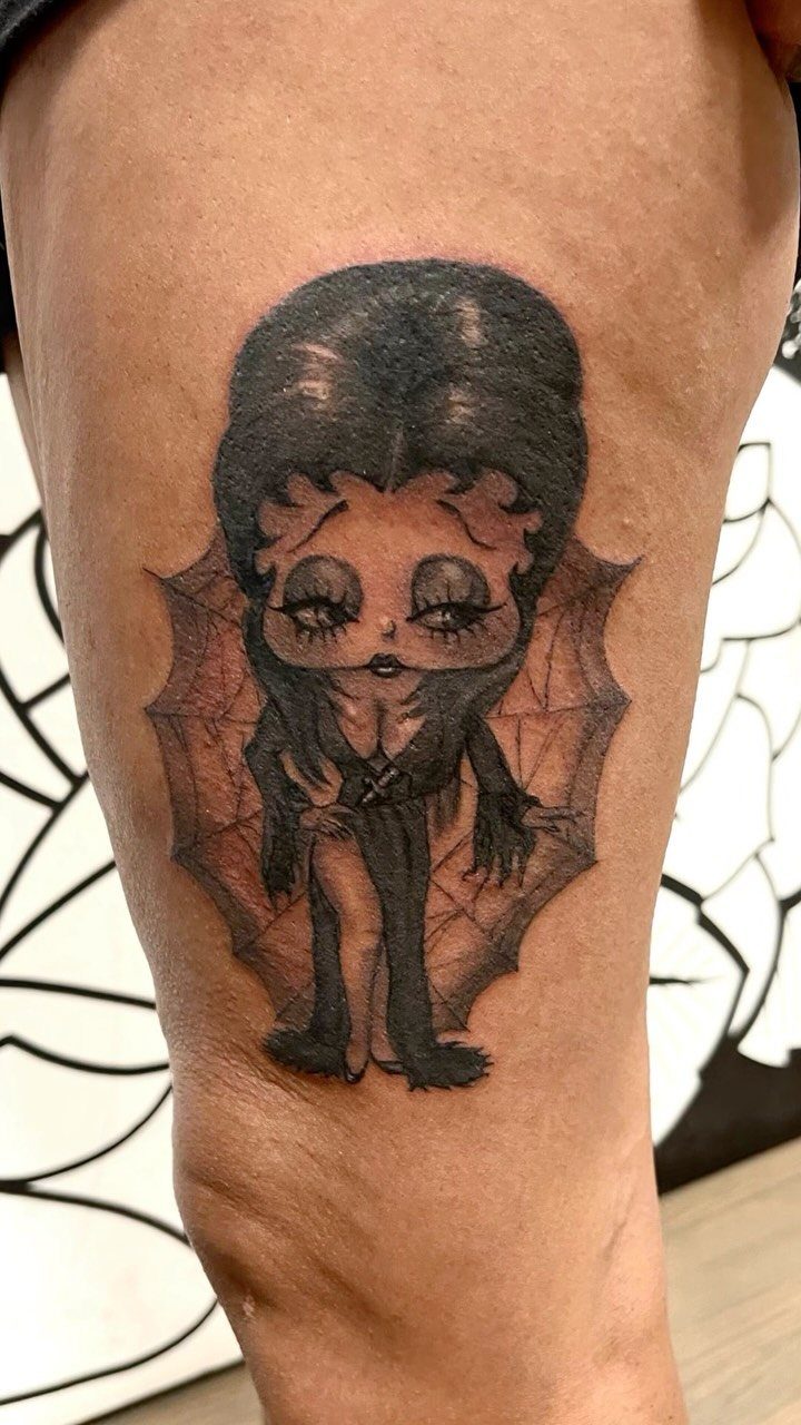 Elvira tattoo with a high beehive hairstyle and spiderweb background on a leg