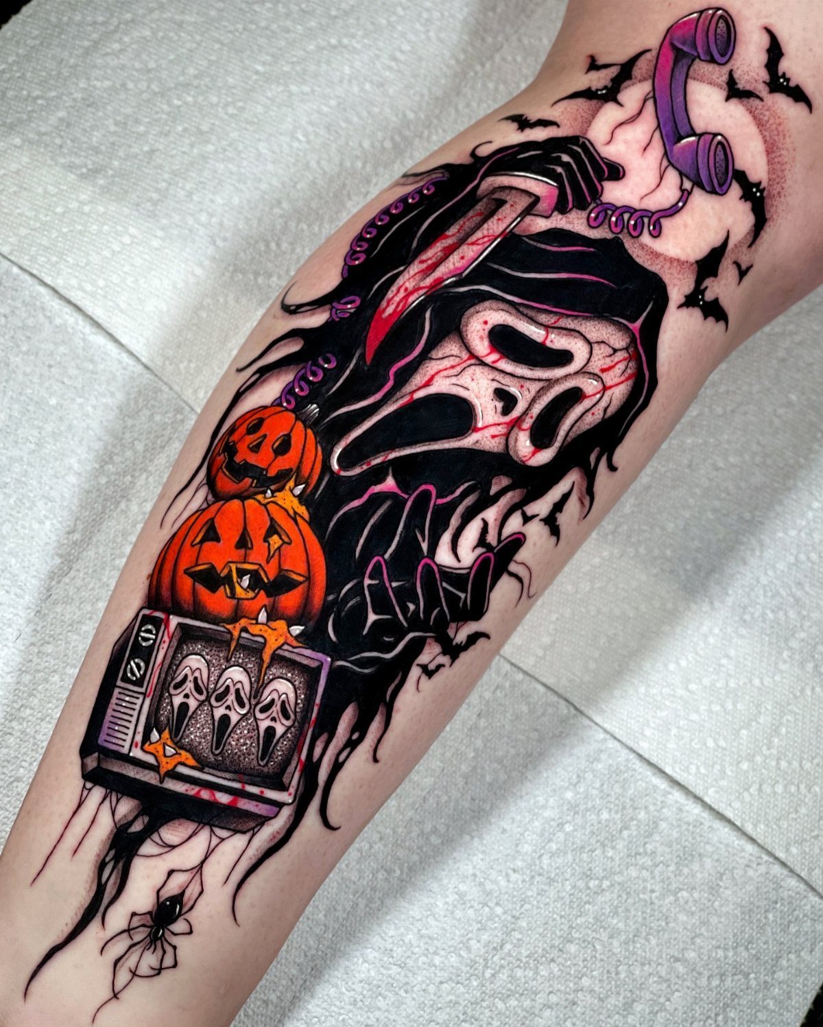 Ghostface tattoo with blood tears, pumpkins, and a purple phone on an arm.