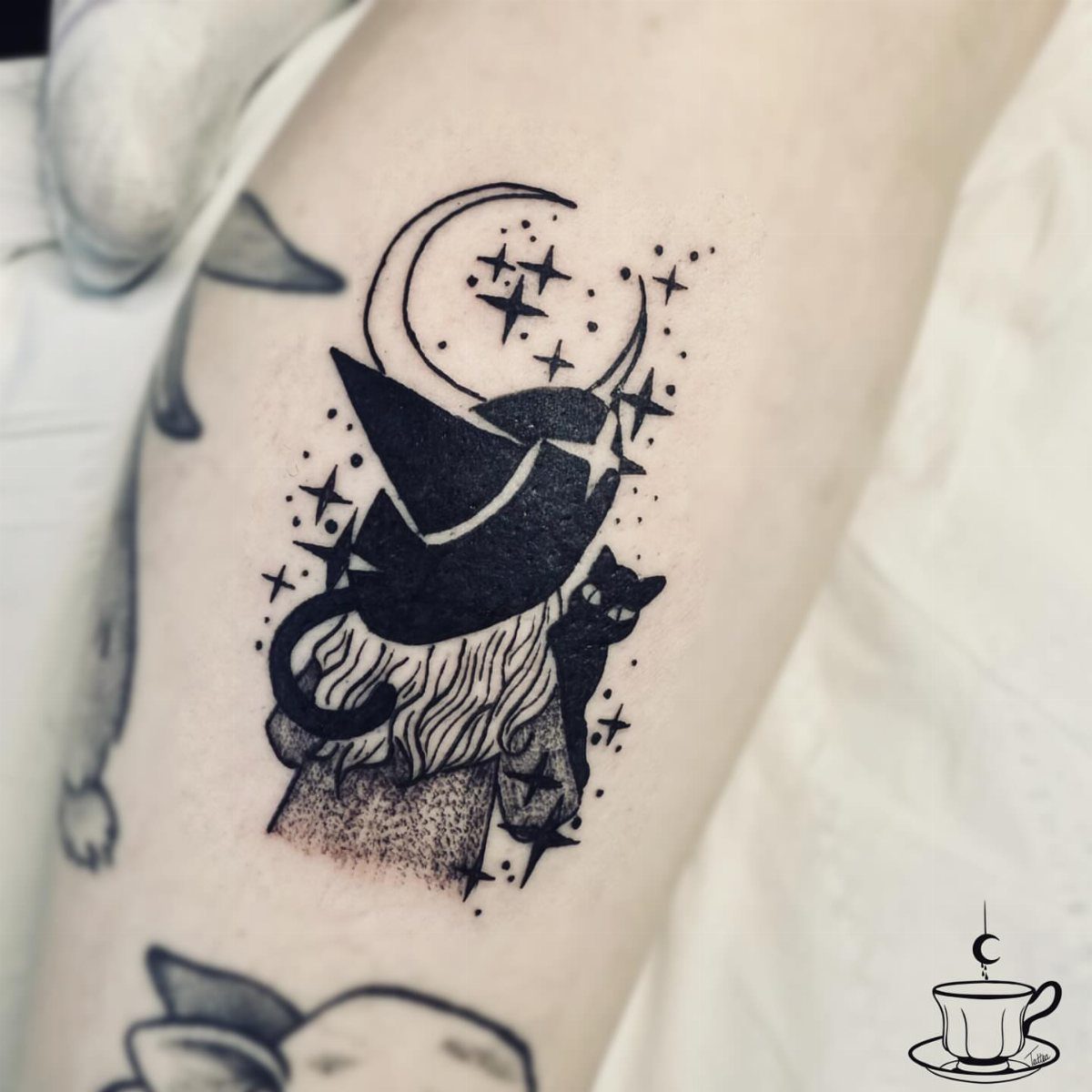 Black cat tattoo wearing a witch hat under a crescent moon and stars.