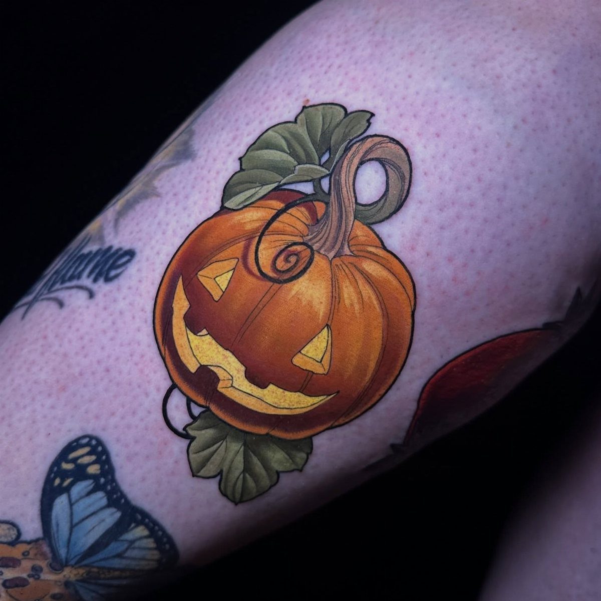 Jack-o'-lantern pumpkin tattoo with green leaves on a person's skin