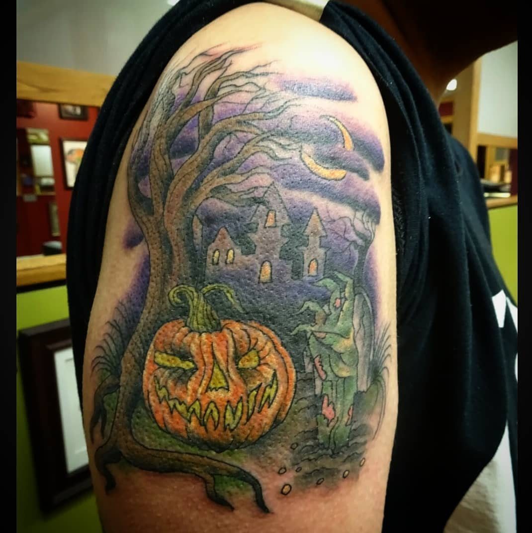 Tattoo of a spooky scene with a gnarled tree, pumpkin, and haunted castle.