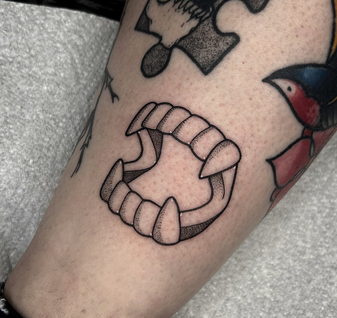 Vampire teeth tattoo with sharp fangs on a person's forearm.
