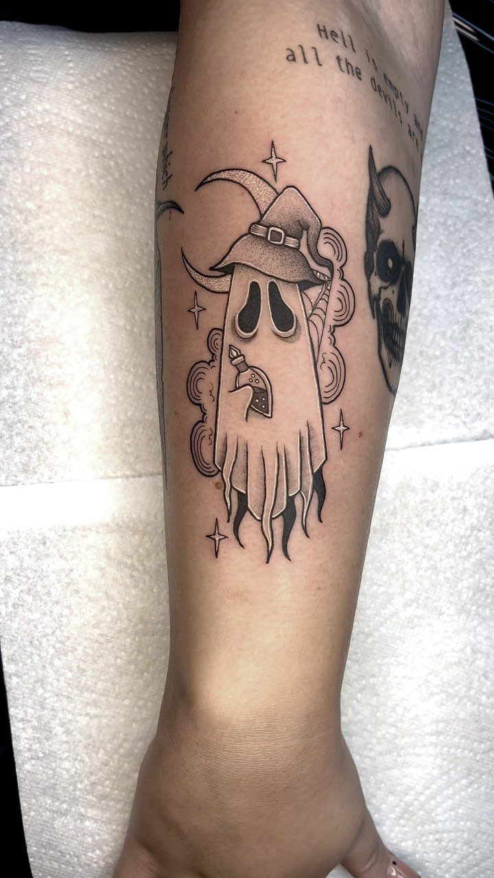 Ghost tattoo wearing a witch hat and holding a candle on a forearm