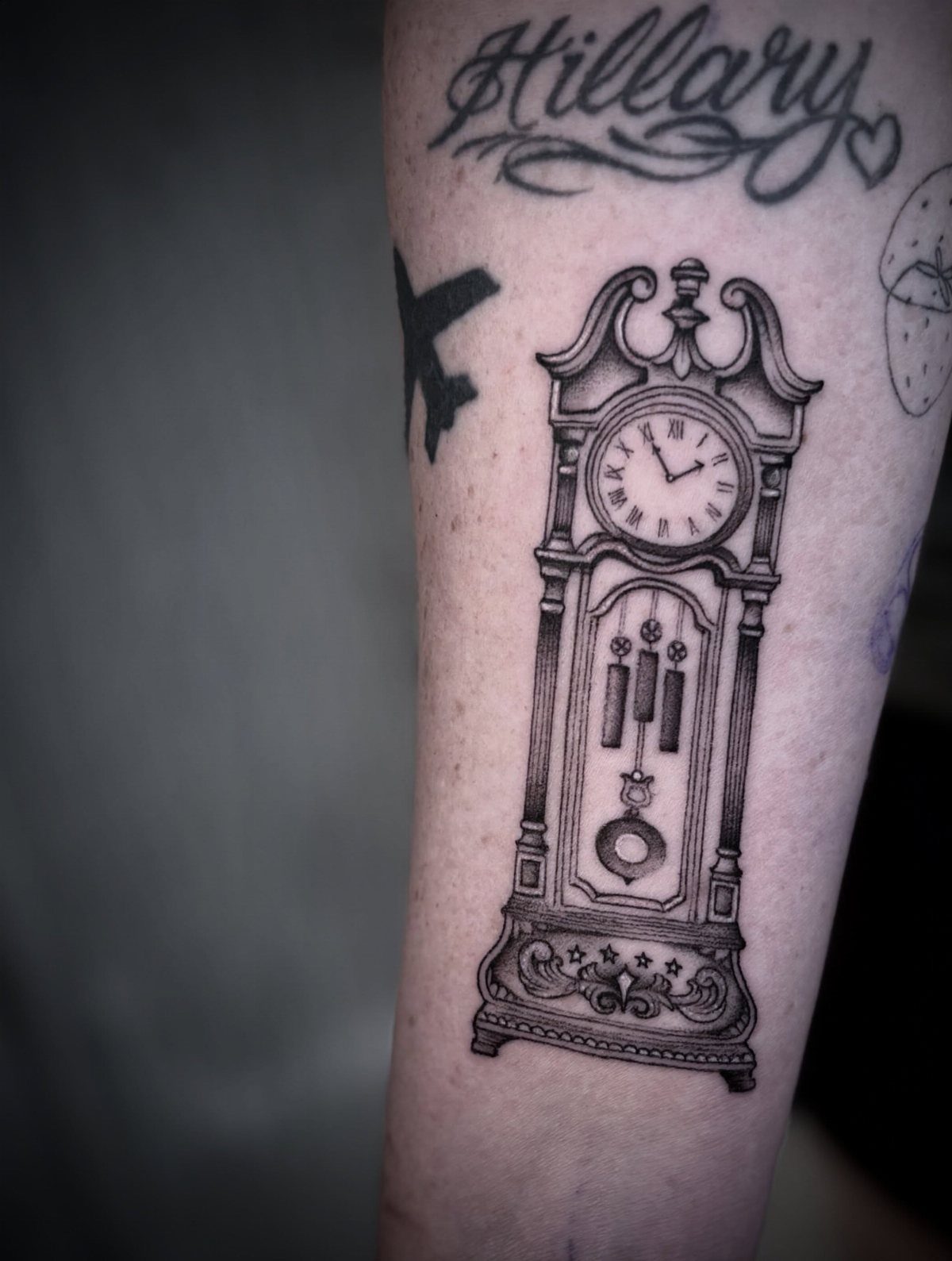 Grandfather clock tattoo with Roman numerals and pendulum on a person's arm.