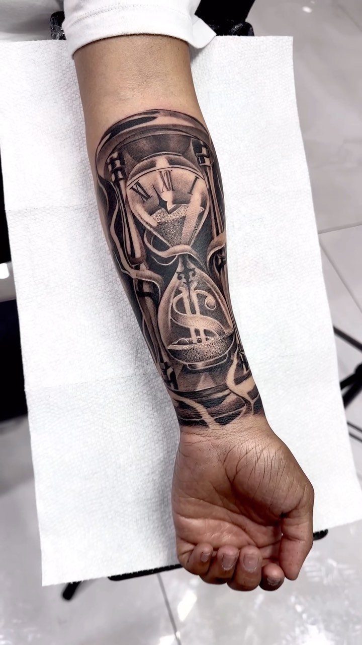Hourglass tattoo on a forearm featuring a figure and a dollar sign.