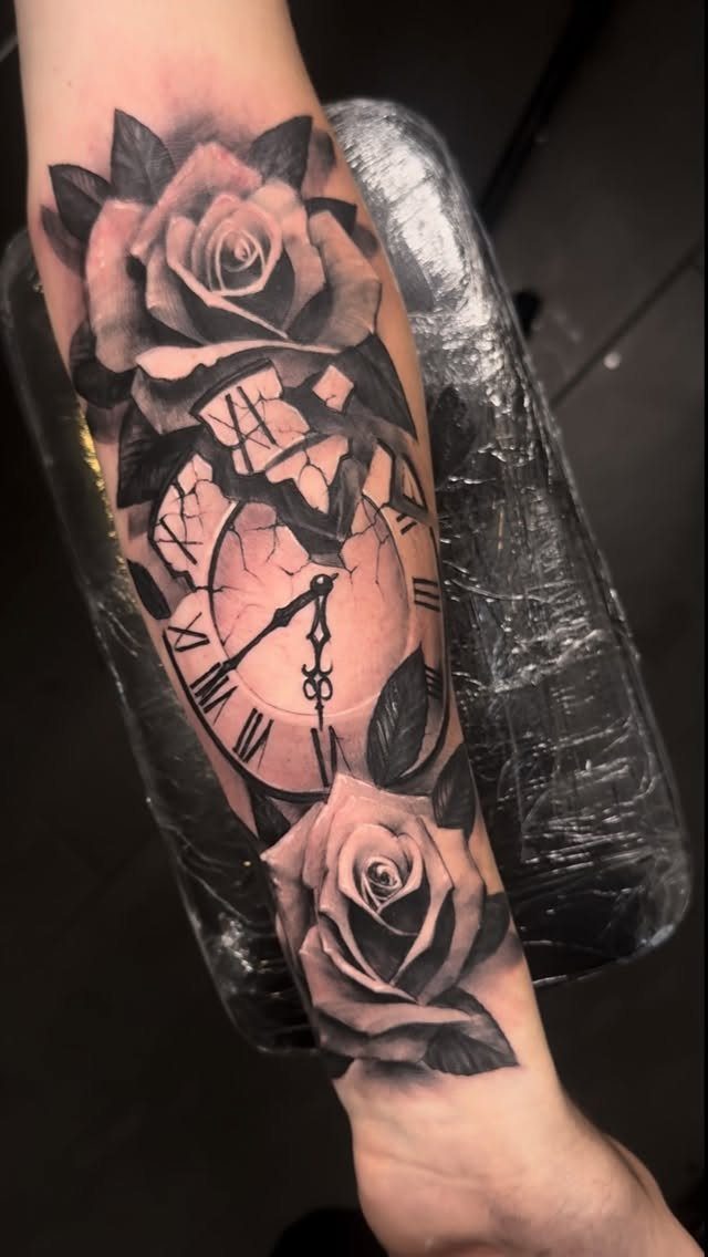Rose clock tattoo on a forearm with a cracked clock face and roses.