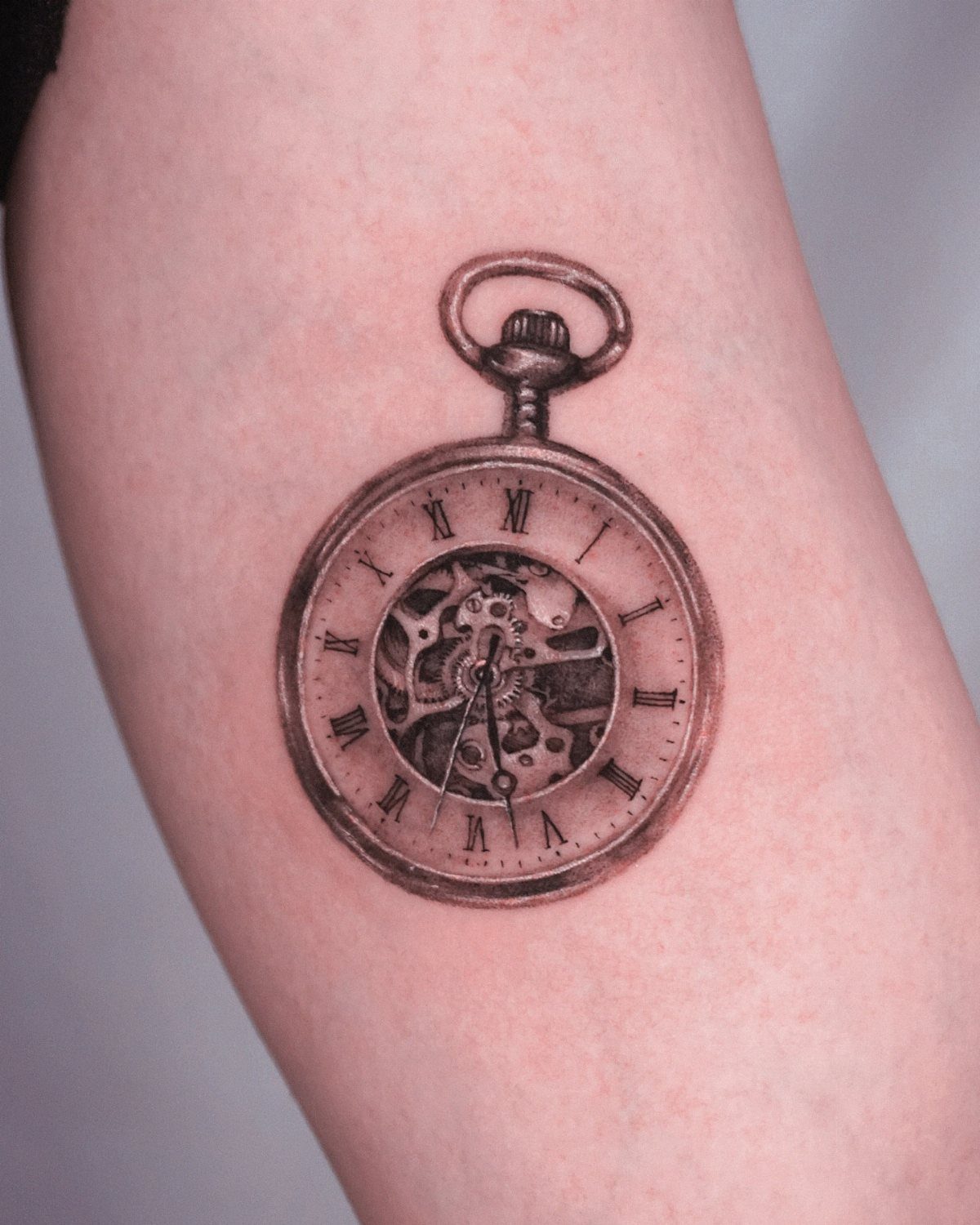 Pocket watch tattoo with Roman numerals and internal gears on skin.