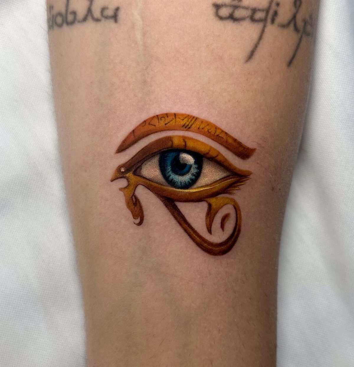 Eye of Horus tattoo with a realistic blue eye and golden Egyptian symbols.