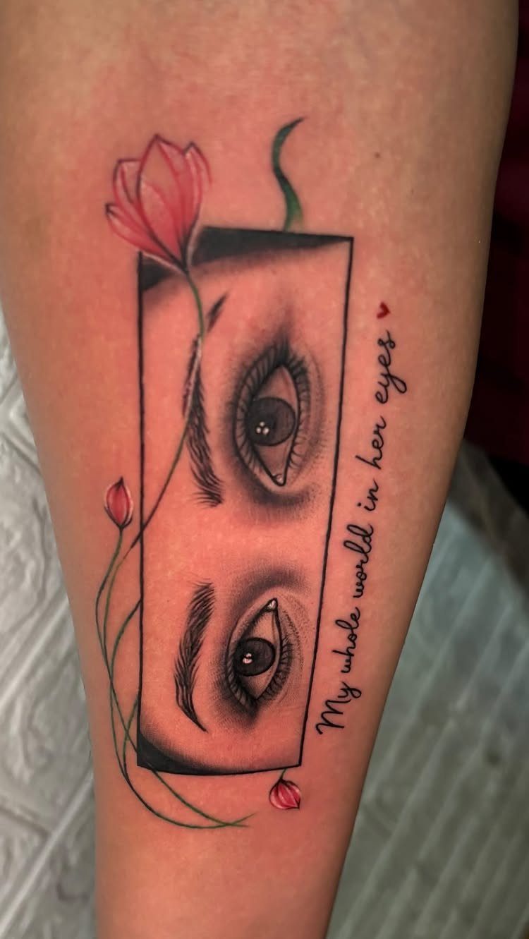 Tattoo of two realistic eyes with pink flowers and cursive script on skin