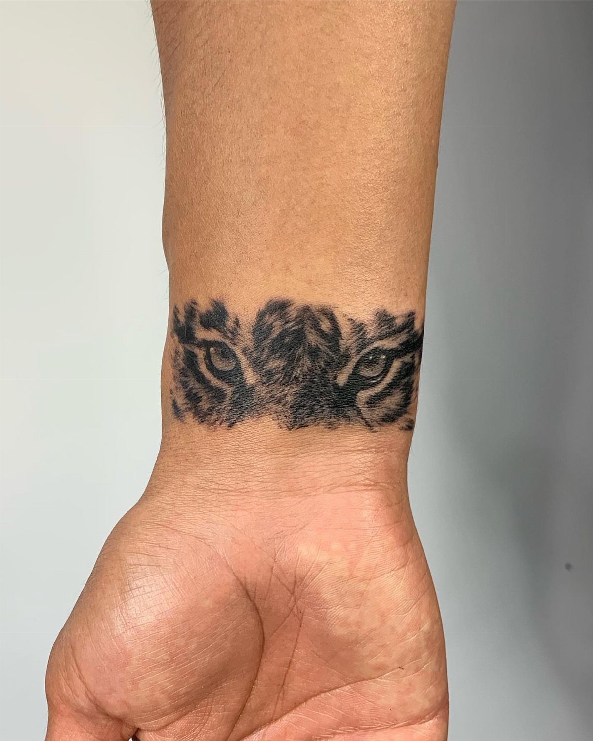 Tiger eyes tattoo wrapped around a person's wrist in black and grey ink.