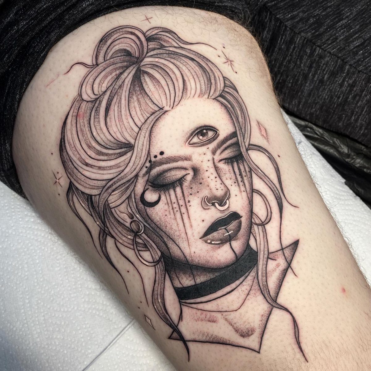 Woman's face tattoo with a third eye open on her forehead in black ink.