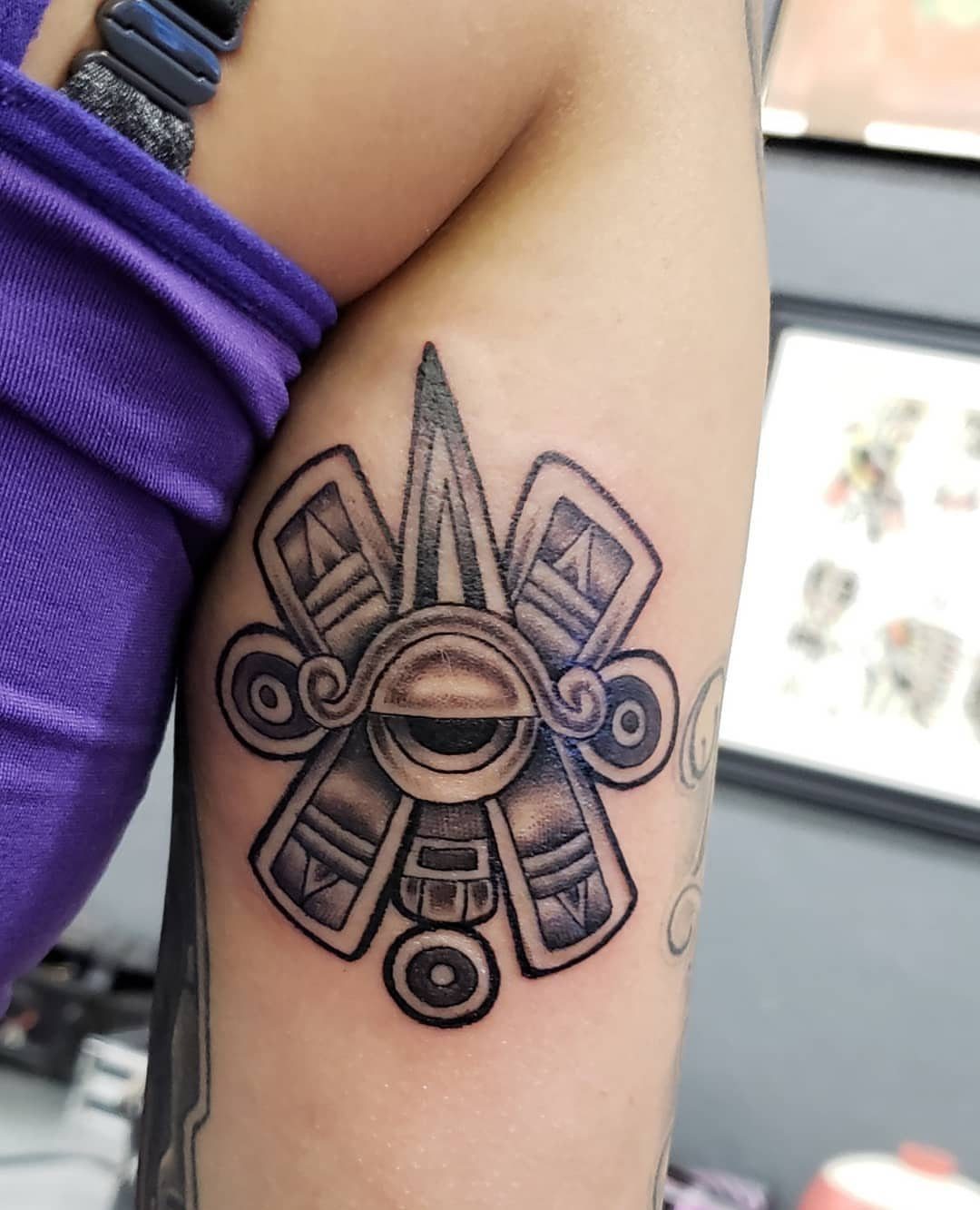 Stylized eye tattoo with geometric patterns and shading on a person's arm.