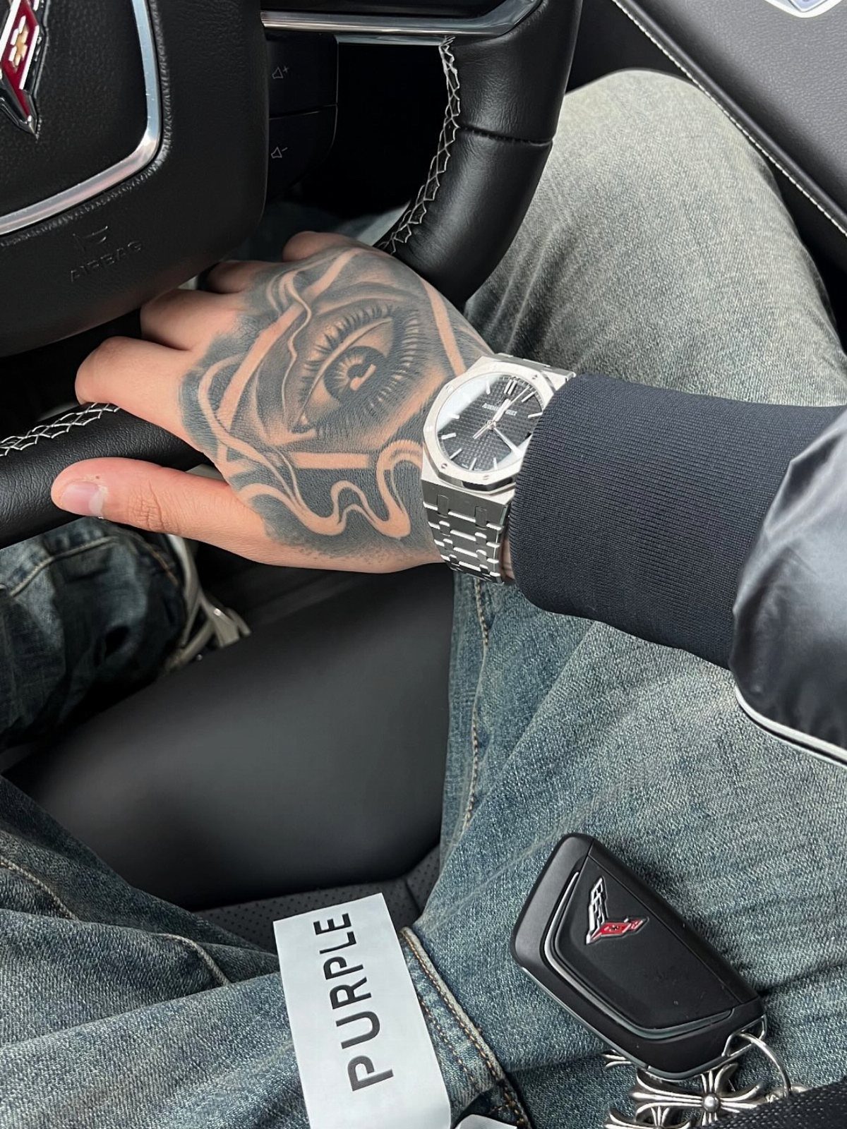 Hand with a realistic eye tattoo holding a car steering wheel
