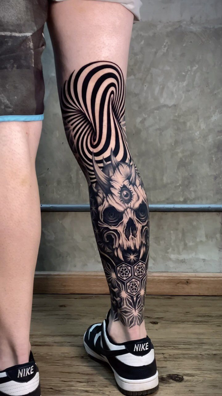 Tattoo on a lower leg featuring a skull with a third eye and spiral.