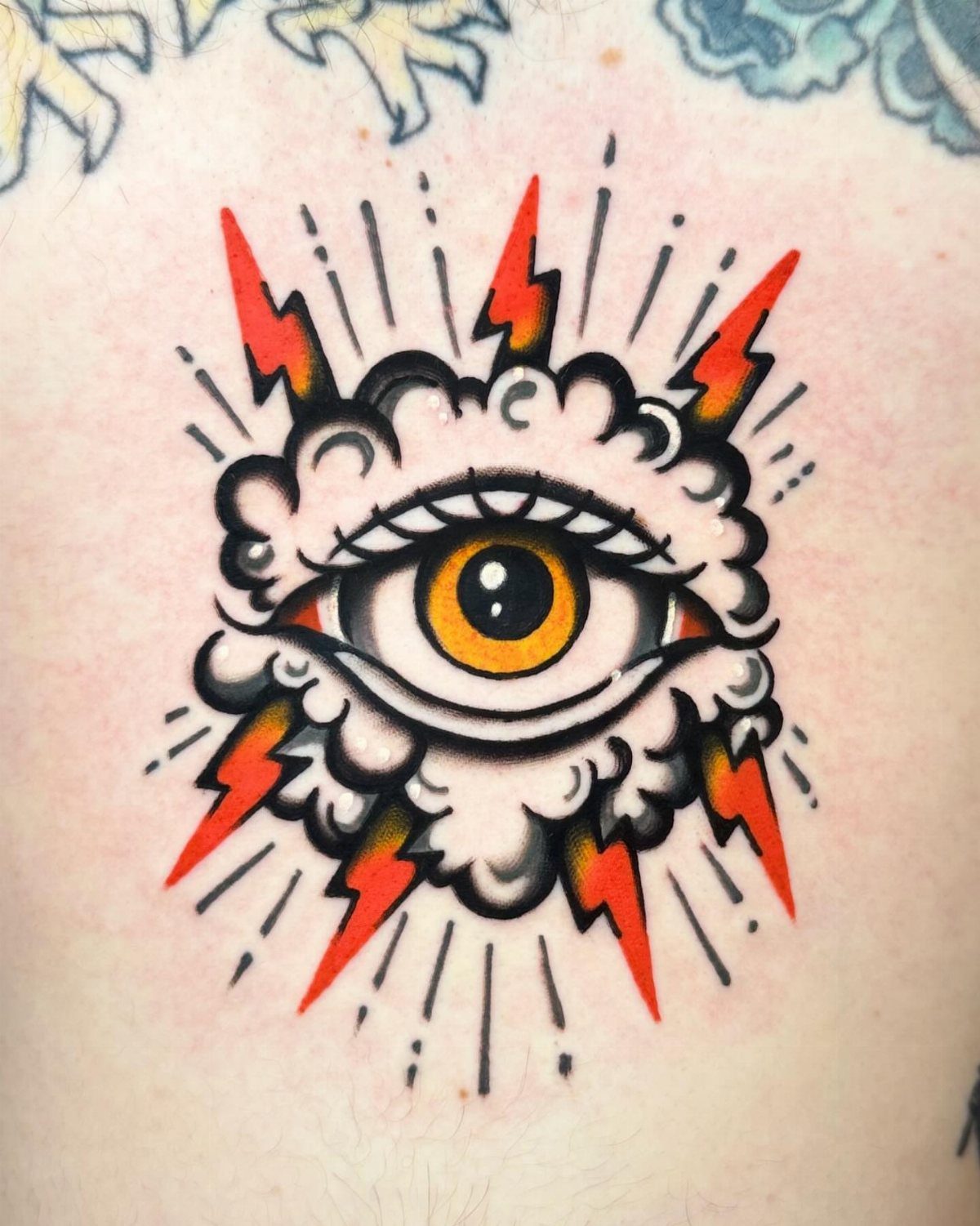Tattoo of a yellow eye in a cloud with red lightning bolts striking outward.