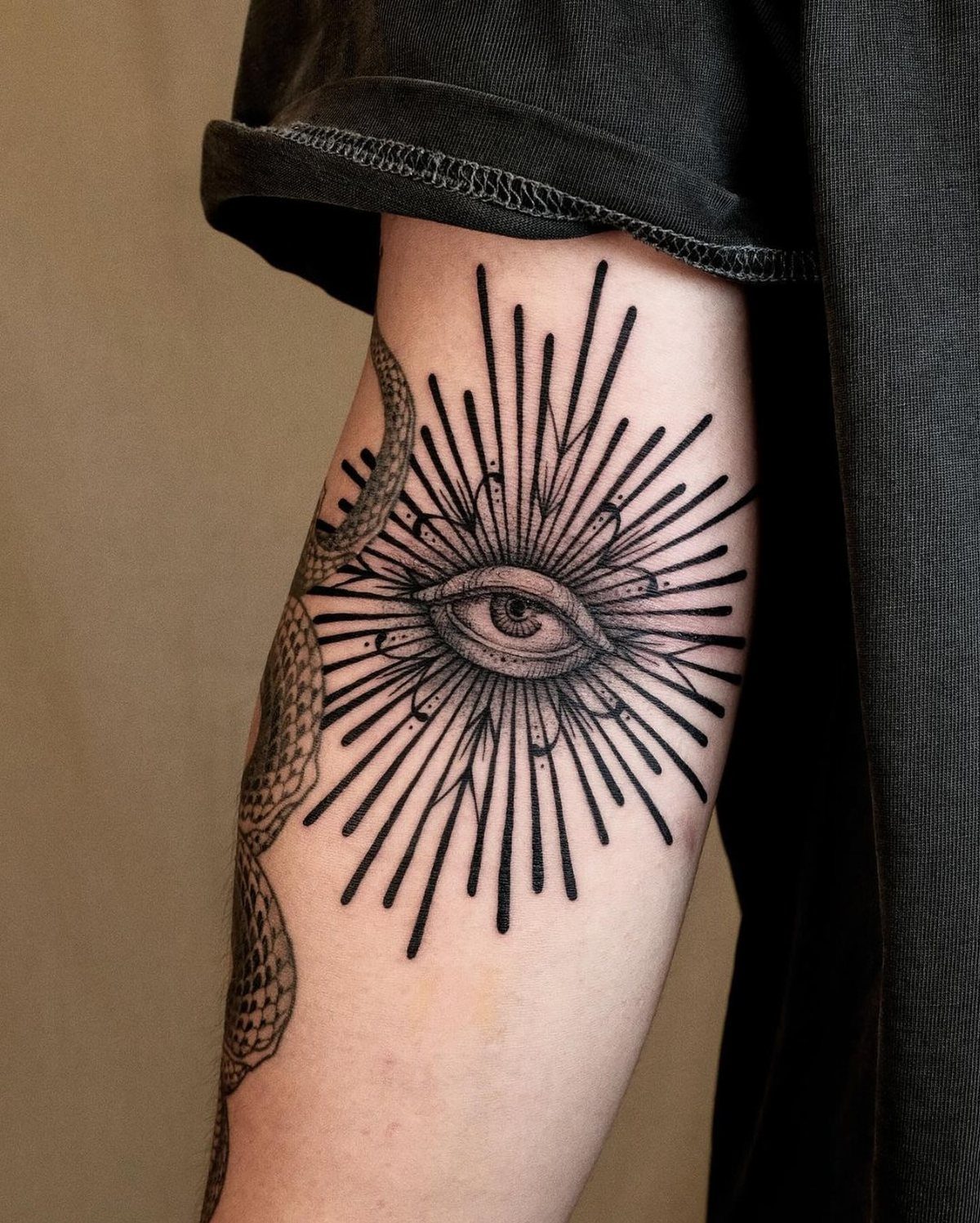 Eye tattoo with radiating lines and a serpent on a person's arm