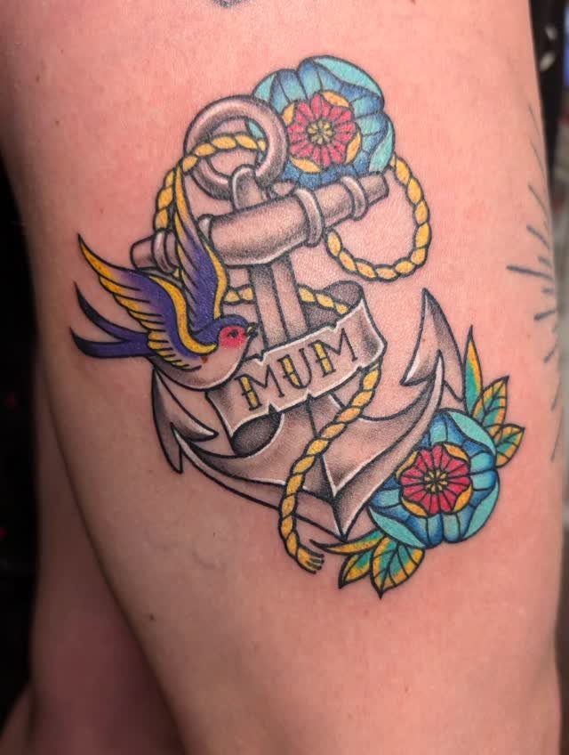 Traditional anchor tattoo with a swallow, flowers, and a banner reading MUM on skin
