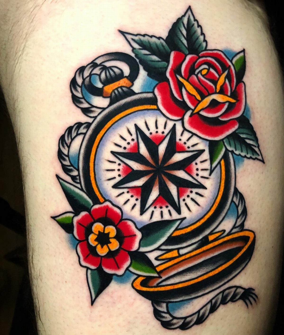 Traditional tattoo of a pocket compass with a red rose and green leaves.