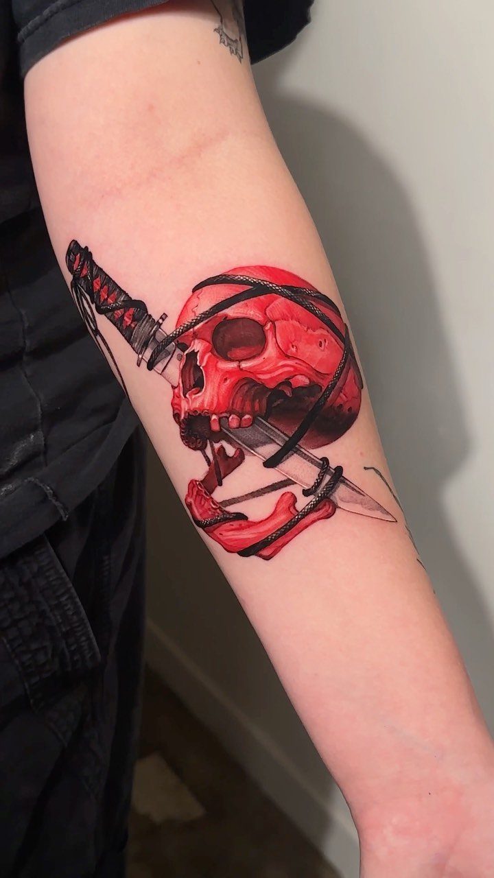 Red skull tattoo with a dagger on a person's forearm