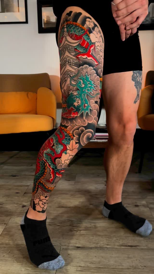 Leg with a traditional red and green dragon tattoo among grey clouds.