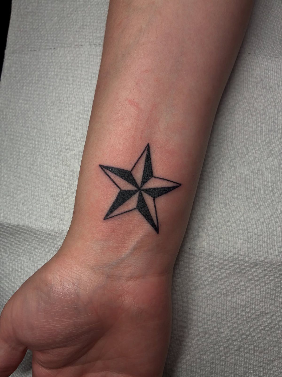 Nautical star tattoo with black and grey shading on a person's inner wrist.