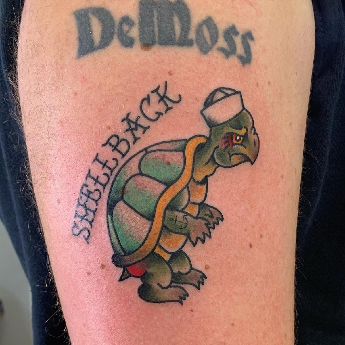 Sailor turtle tattoo with the word Shellback on a person's upper arm