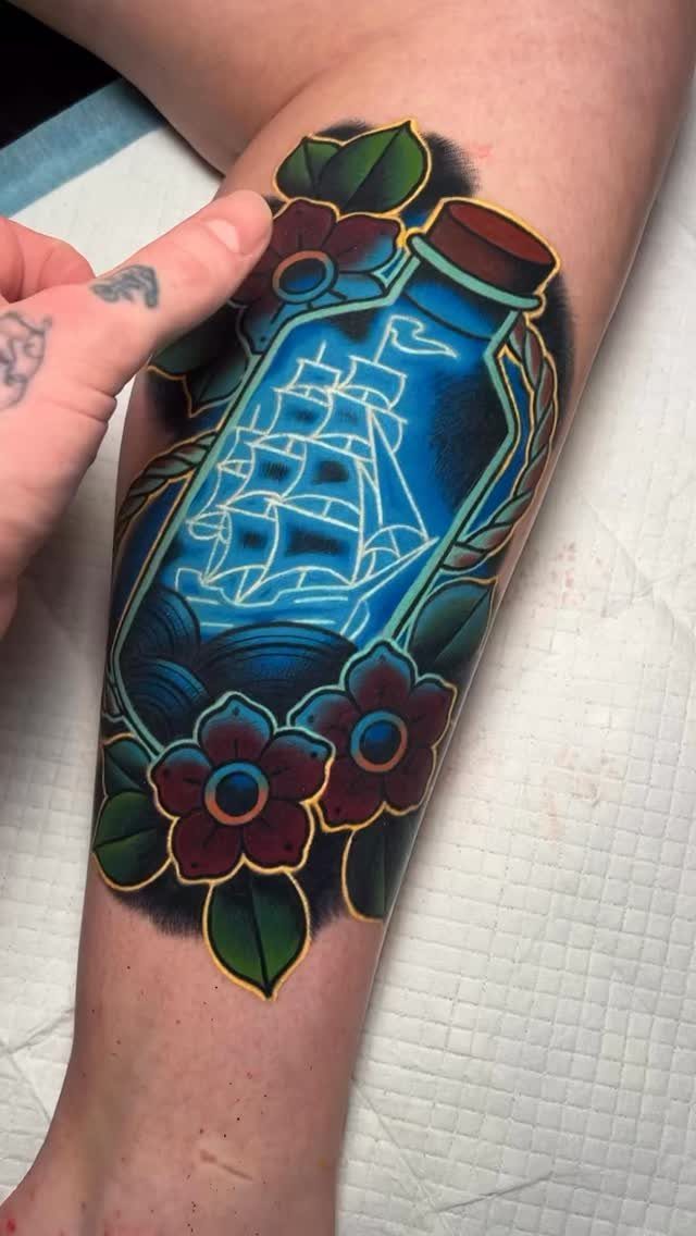 Traditional tattoo of a sailing ship inside a blue bottle with red flowers