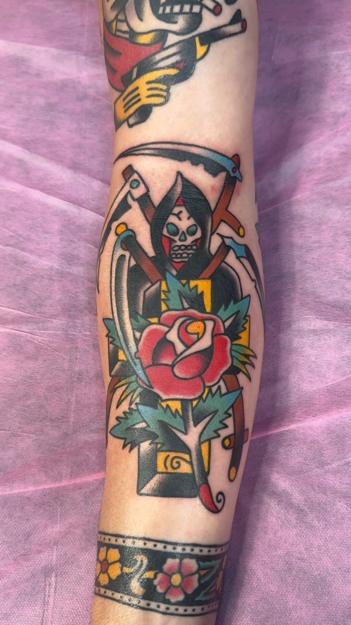 Grim reaper skull and red rose traditional tattoo on a person's forearm