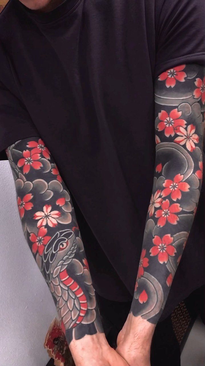 Sleeve tattoos featuring a large snake and red cherry blossoms on a person's arms.