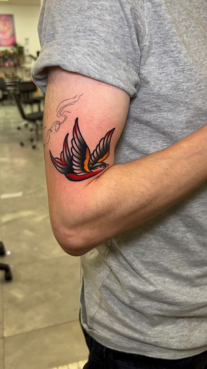 Traditional swallow tattoo with red and yellow accents on a person's upper arm.